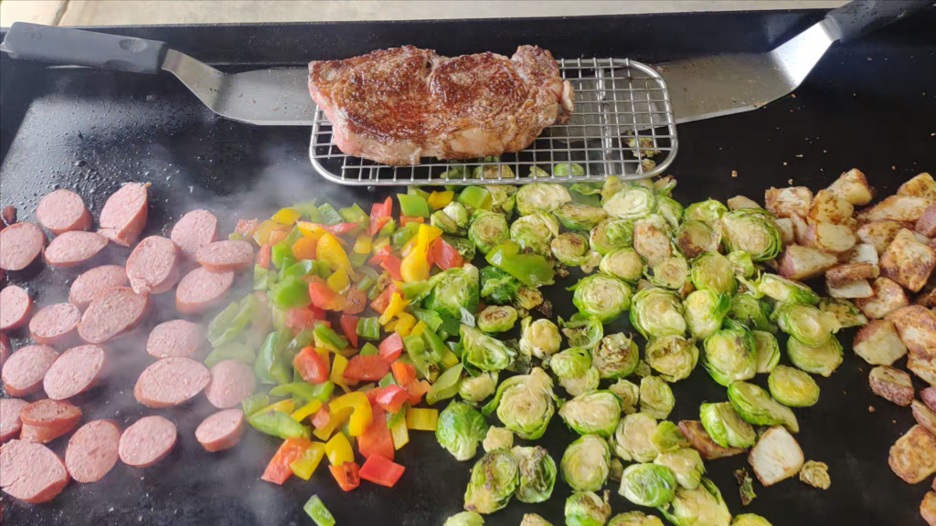 steak, keilbasa, brussel sprouts and potatoes on a griddle