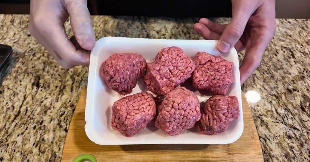 6 ground beef balls in a white styrofoam container.  Sitting on a cutting board being held by two hands.